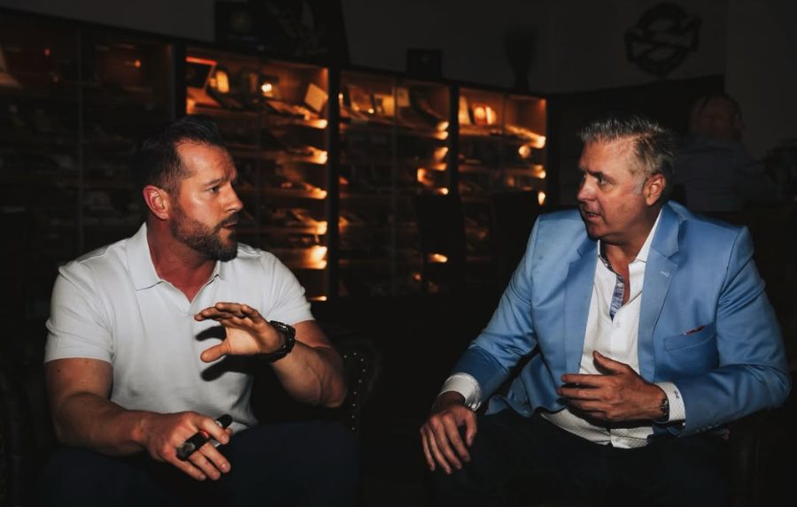 Two members in conversation beside a lit humidor